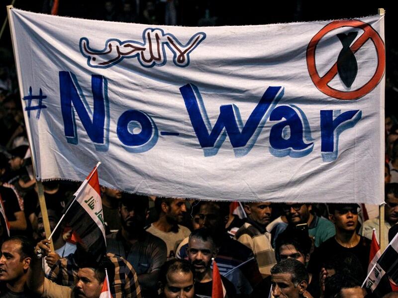 Iraqi followers of Shiite Muslim cleric Moqtada al-Sadr wave national flags and raise protest signs as they demonstrate in the capital Baghdad's central Tahrir Square late on May 24, 2019, against involvement in any conflict between Iran and the United States.  AHMAD AL-RUBAYE / AFP