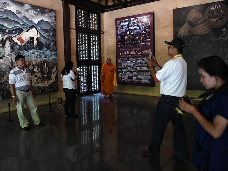 This picture taken on June 13, 2019 shows visitors taking photos in front of artwork illustrating the rescue of the 12 boys from the "Wild Boars" football team and their coach, who were trapped in the Tham Luang cave last year, at the cave's visitor centre in the Mae Sai district of Chiang Rai province. Lillian SUWANRUMPHA / AFP