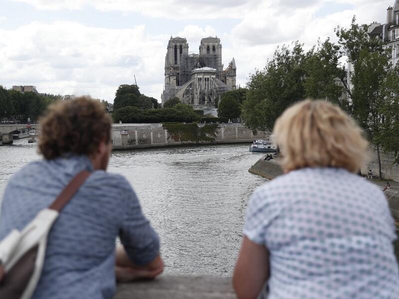 People stand on the river bank as they look towards the Notre-Dame de Paris cathedral on June 15, 2019. Zakaria ABDELKAFI / AFP