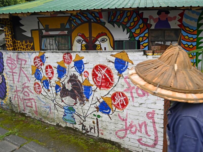 This picture taken on March 30, 2019 shows a local resident walking past a house painted by Hakka graffiti artist Wu Tsun-hsien in the Taiwanese village of Ruan Chiao. Nestled in the mist-covered foothills of Taiwan's central mountain range, Ruan Chiao village is virtually devoid of young people, but artist Wu Tsun-hsien is coaxing the Instagram generation back by transforming local homes into a canvas of colour. Sam YEH / AFP
