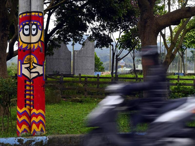 This picture taken on March 30, 2019 shows an motorcyclist riding past a utility pole painted by Hakka graffiti artist Wu Tsun-hsien in the Taiwanese village of Ruan Chiao. Nestled in the mist-covered foothills of Taiwan's central mountain range, Ruan Chiao village is virtually devoid of young people, but artist Wu Tsun-hsien is coaxing the Instagram generation back by transforming local homes into a canvas of colour. Sam YEH / AFP