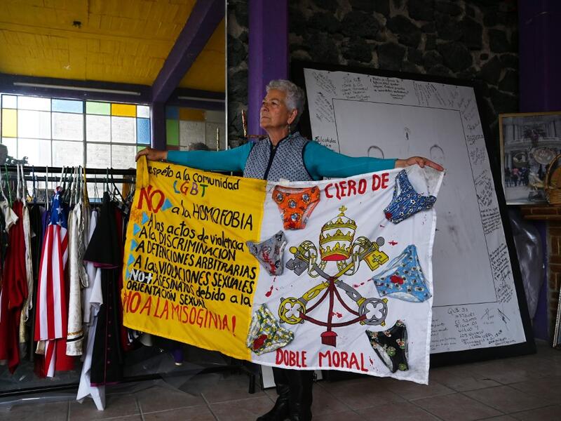 Mexican activist Julia Klug poses with a banner against homophobia in Mexico City on August 08, 2019. Pork masks, a giant magnifying glass made with a sewing drum, and hundreds of costumes are included in the collection of Julia Klug. RODRIGO ARANGUA / AFP