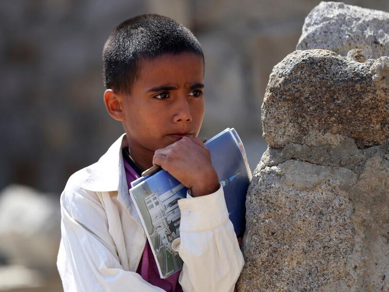 A Yemeni boy holds his notebooks as school children attend an open-air class under a tree near their unfinished school  Ahmad AL-BASHA / AFP
