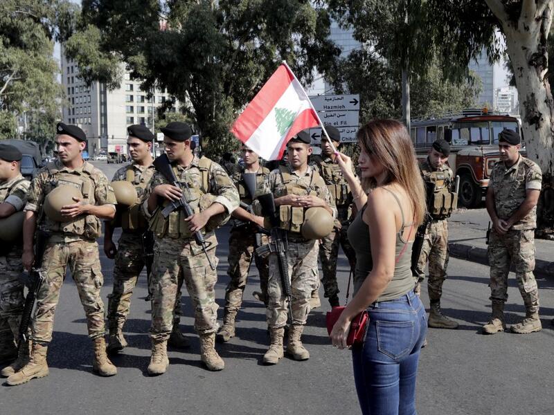 A Lebanese woman waves a national flag in front of soldiers standing guard on a main road in the eastern outskirts of the capital Beirut on October 22, 2019. Lebanese protesters gathered for a sixth consecutive day today, keeping the country on lockdown to demand new leaders despite the government's adoption of an emergency economic rescue plan.  ANWAR AMRO / AFP