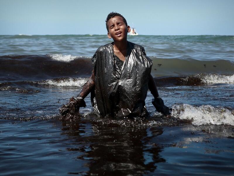 A boy walks out of the sea while removing oil spilled on Itapuama beach located in the city of Cabo de Santo Agostinho, Pernambuco state, Brazil, on October 21, 2019. LEO MALAFAIA / AFP