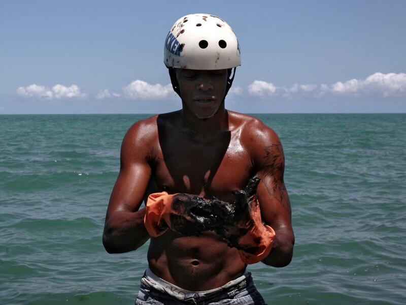 A volunteer removes crude spilled at Janga beach in Paulista, Pernambuco state, Brazil, on October 23, 2019. Large blobs of oil staining more than 130 beaches in northeastern Brazil began appearing in early September and have now turned up along a 2,000km stretch of the Atlantic coastline. Leo Malafaia / AFP