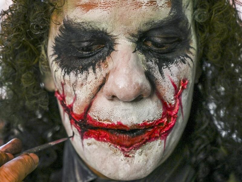 Venezuelan migrant Johnny Tales (R), who makes a living imitating the comicbook and film character "The Joker", applies make up as he prepares to work in downtown Medellin, on October 28, 2019. JOAQUIN SARMIENTO / AFP