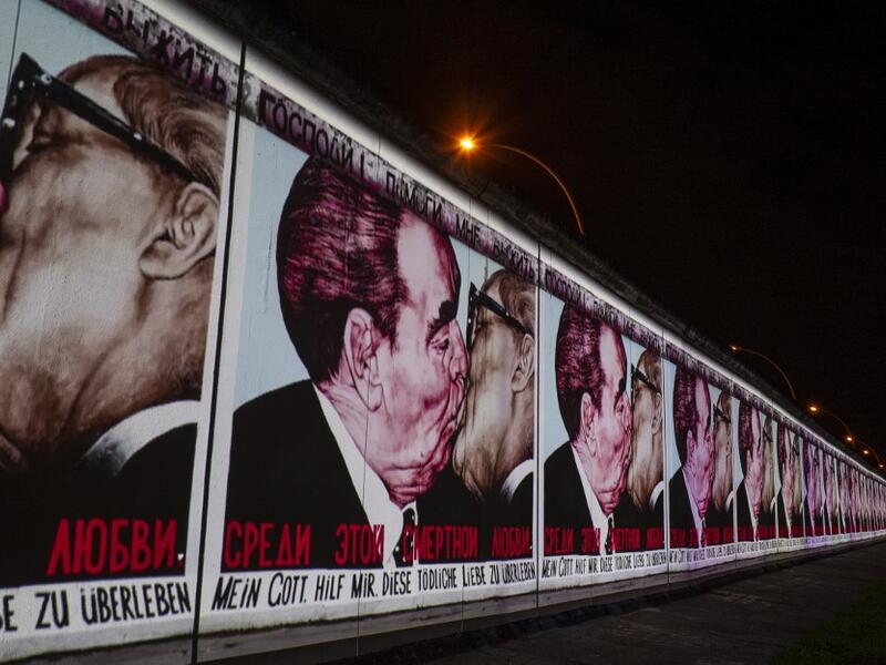 The mural painting "My God, Help Me to Survive This Deadly Love" by Russian painter Dmitri Vrubel, depicting the kiss between then Soviet leader Leonid Brezhnev (L) and East German leader Erich Honecker is projected on a stretch of the Berlin wall at the so-called East-side Gallery during the city-wide kick-off of the festival week to celebrate the 30th anniversary of the November 9,1989 fall of the Berlin Wall, in Berlin on November 4, 2019. Germany marks three decades since the fall of the Berlin Wall thi