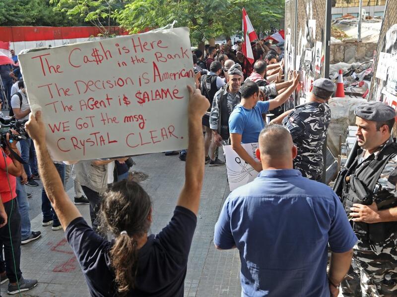 An anti-government protester holds a placard as others break down a construction barrier at the entrance of Lebanon's Central Bank during a rally at the same time of a press conference held by the bank's governor in Beirut on November 11, 2019. (AFP/ File Photo)1