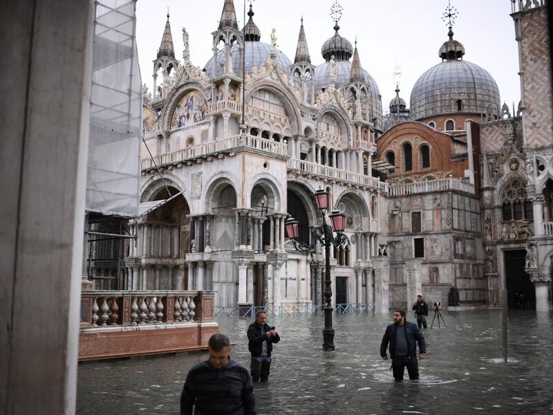 People wearing thigh boots cross flooded St. Mark's square by St. Mark's Basilica after an exceptional overnight "Alta Acqua" high tide water level Marco Bertorello / AFP