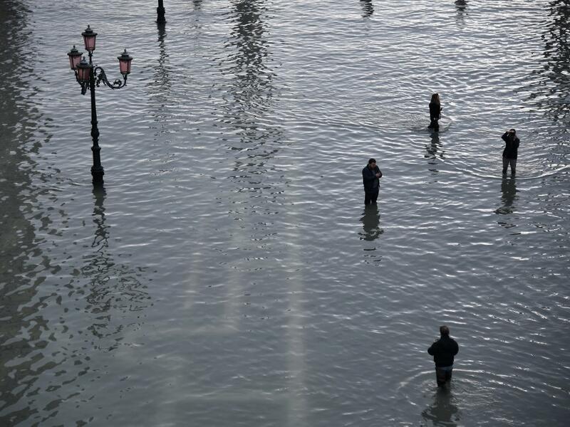 People walk across and take photos at the flooded St. Mark's Square after an exceptional overnight "Alta Acqua" high tide water level, on November 13, 2019 in Venice. Venice was hit by the highest tide in more than 50 years late November 12, with tourists wading through flooded streets to seek shelter as a fierce wind whipped up waves in St. Mark's Square. Marco Bertorello / AFP