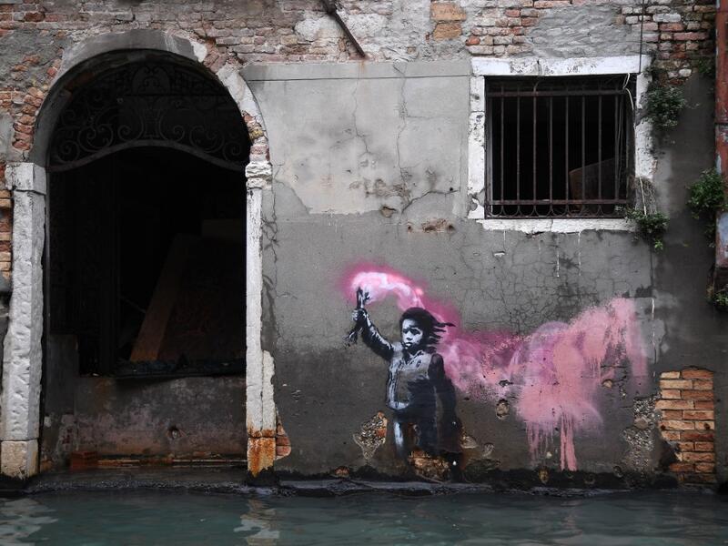 The artwork by street artist Banksy, that portrays a migrant child wearing a lifejacket and holding a neon pink flare, is pictured after an exceptional overnight "Alta Acqua" high tide water level, on November 13, 2019 in Venice. Venice was hit by the highest tide in more than 50 years late November 12, with tourists wading through flooded streets to seek shelter as a fierce wind whipped up waves in St. Mark's Square. Marco Bertorello / AFP