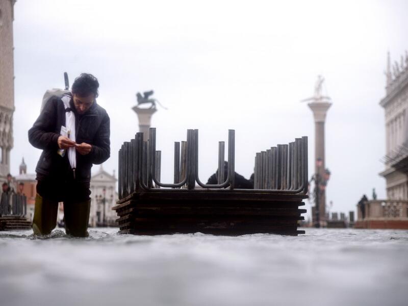 A man prepares a cigarette as he walks in the water of the flooded St. Mark's Square, on November 15, 2019 in Venice, two days after the city suffered its highest tide in 50 years. Flood-hit Venice was bracing for another exceptional high tide on November 15, as Italy declared a state of emergency for the UNESCO city where perilous deluges have caused millions of euros worth of damage. Filippo MONTEFORTE / AFP