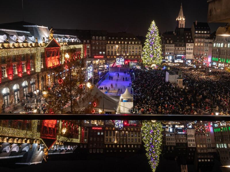 This picture shows a reflected view of the city's illuminated main square and Christmas tree as people gather on the opening day of the 450th traditional Christmas market in Strasbourg, eastern France, one year after the deadly attack that killed five people.  PATRICK HERTZOG / AFP