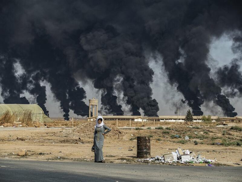 AFP PICTURES OF THE YEAR 2019 - A woman stands along the side of a road on the outskirts of the town of Tal Tamr near the Syrian Kurdish town of Ras al-Ain along the border with Turkey in the northeastern Hassakeh province on October 16, 2019, with the smoke plumes of tire fires billowing in the background to decrease visibility for Turkish warplanes during the continuing deadly cross-border Turkish offensive against Syria's Kurdish forces that has sparked an international outcry. Delil SOULEIMAN / AFP
