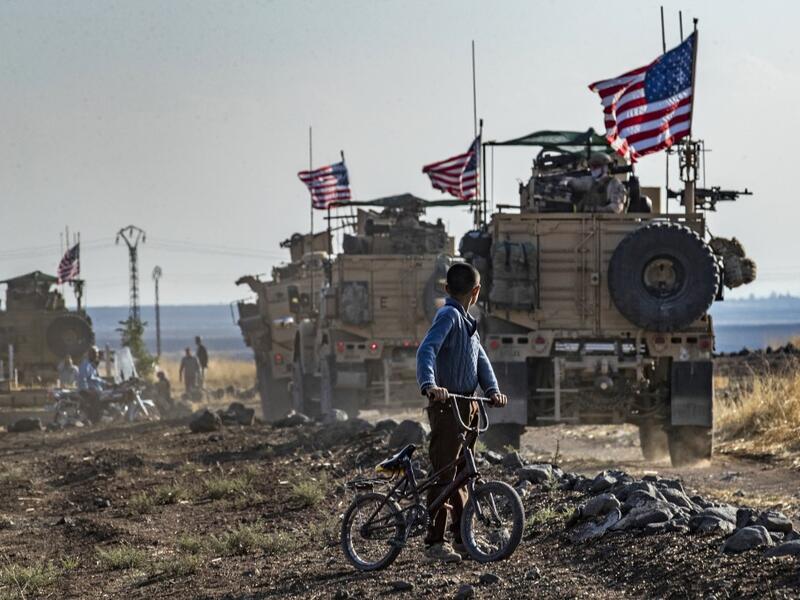 A Syrian boy on his bicycle looks at a convoy of US armoured vehicles patrolling fields near the northeastern town of Qahtaniyah at the border with Turkey (AFP)