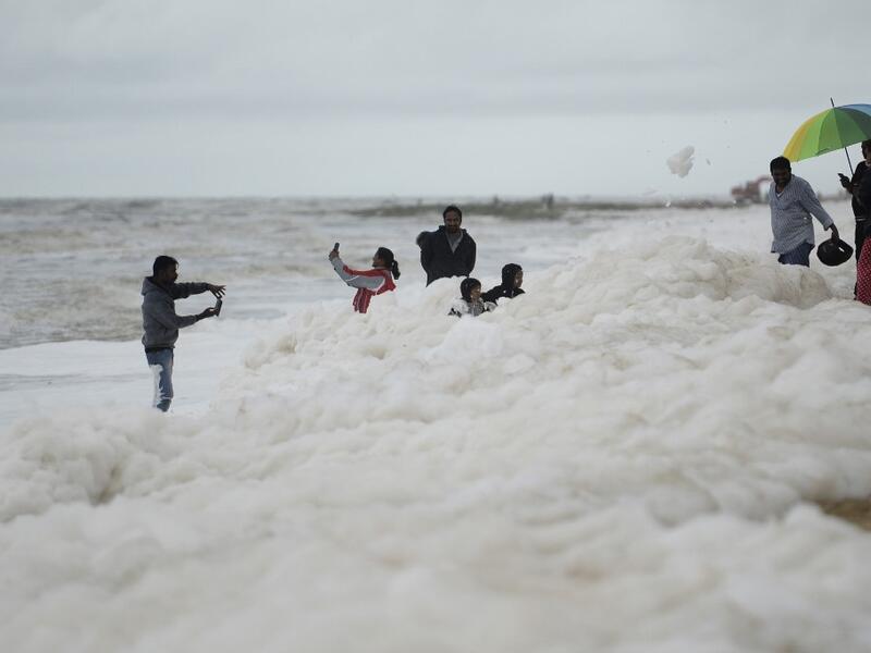Residents take selfie pictures as foamy discharge, caused by pollutants, mix with surf at Marina beach in Chennai on December 1, 2019. Arun SANKAR / AFP