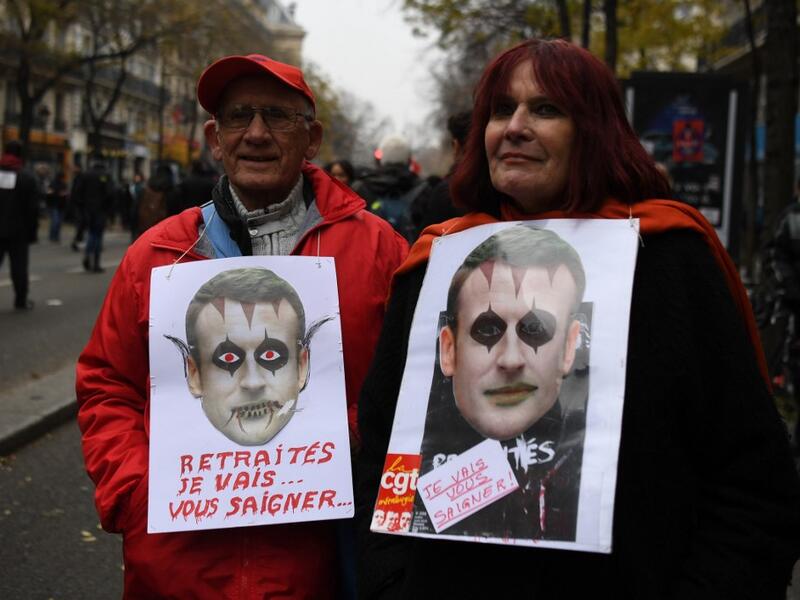 A man and a woman hold signs reading "Pensioners, I will bleed you" and bearing pictures mocking French President Emmanuel Macron during a demonstration against the pension overhauls, in Paris, on December 5, 2019 as part of a nationwide strike. ALAIN JOCARD / AFP