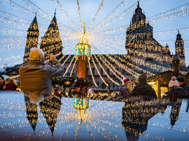 A man photographs the cathedral and the festive lighting of the Christmas market as they mirror on a polished surface in Mainz, Germany, on December 6, 2019.  Frank Rumpenhorst / dpa / AFP