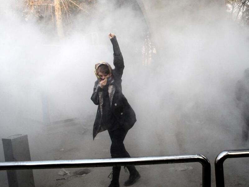 An Iranian woman raises her fist amid the smoke of tear gas at the University of Tehran during a protest driven by anger over economic problems, in the capital Tehran. (AFP/ File Photo)