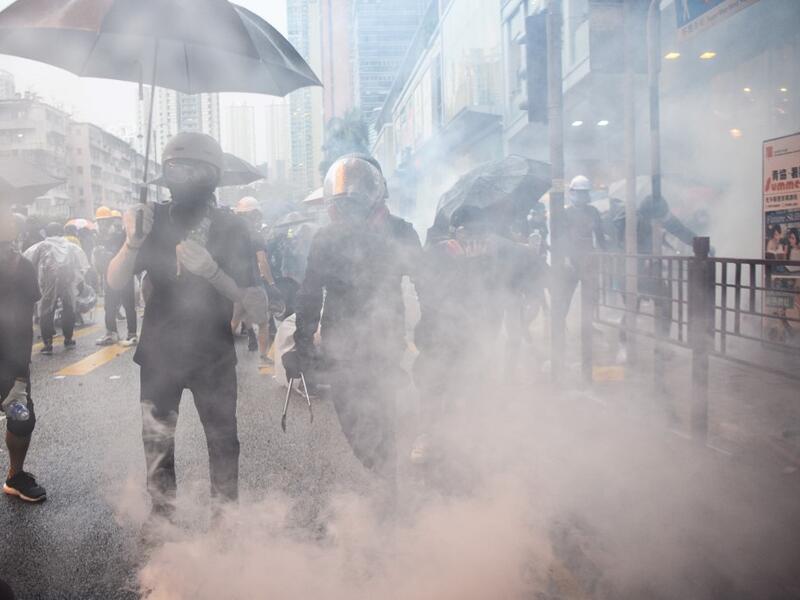 In this picture taken on August 25, 2019, Abby (centre R), 19, and her boyfriend Nick (centre L, holding tongs), 20, react after police fired tear gas during a protest in Tsuen Wan, an area in the New Territories in Hong Kong. ANTHONY WALLACE / AFP