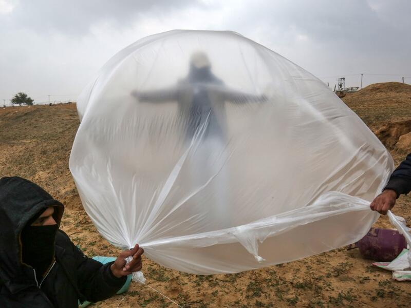 Young Palestinian men, masked in order to avoid being recognised, prepare a flammable object to be flown toward Israel, near the Israel-Gaza border east of Rafah in the southern Gaza Strip, on January 18, 2020. SAID KHATIB / AFP