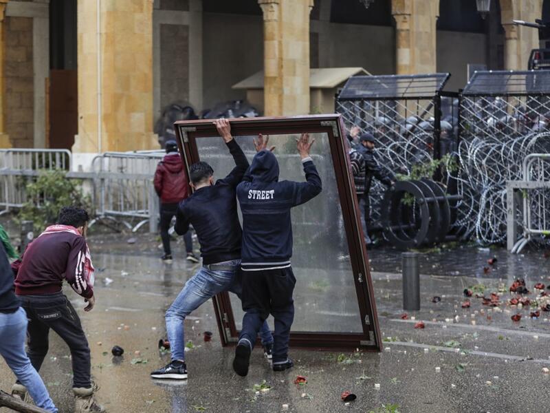 Anti-government protesters use a window as a makeshift shield as they confront security forces from behind a barbed-wire and metal fence barrier during clashes in the central downtown district of the Lebanese capital Beirut near the parliament headquarters on January 18, 2020. ANWAR AMRO / AFP
