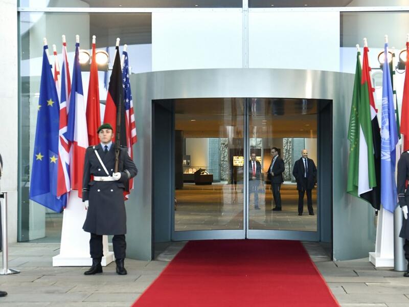 Guards stand next to the flags of the participating countries at the entrance of the German Chancellery in Berlin on January 19, 2020. AFP/ File