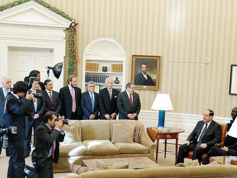 Prime Minister Nouri al-Maliki of Iraq and United States President Barack Obama (seated behind lamp) US President Barack Obama meets Prime Minister Nouri al-Maliki of Iraq at the Oval Office on December 12, 2011. Hadi al Amiri is seen behind the sofa, wearing a blue tie (Shutterstock)	