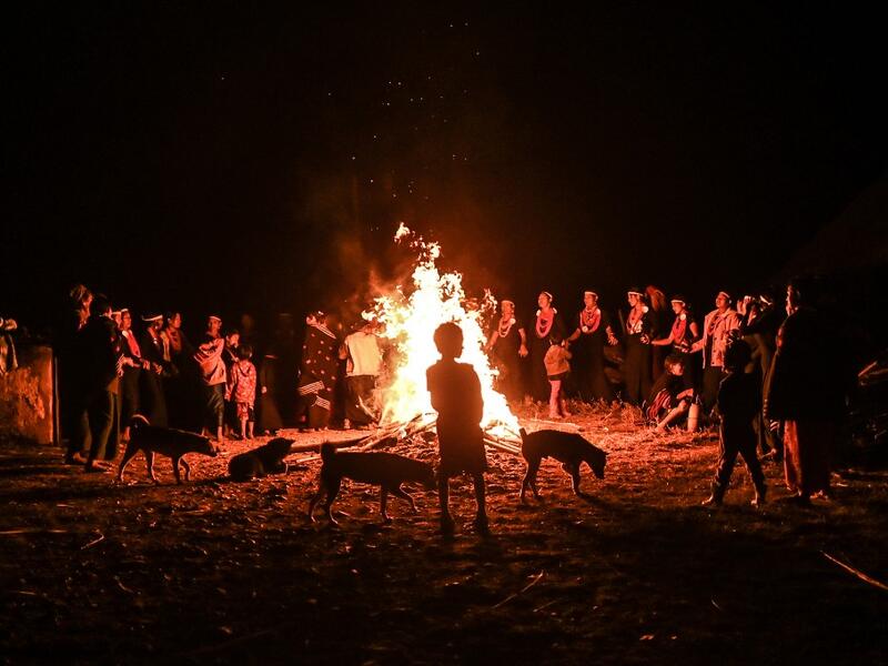 This photo taken on February 6, 2020 shows a child standing with dogs by a fire as Naga tribeswomen take part in an overnight ceremony to bless the harvest in Satpalaw Shaung village, Lahe township in Myanmar's Sagaing region. A haunting refrain pierces the night as the tribeswomen of the Gongwang Bonyo, among the most isolated people in Myanmar, dance around a campfire to bless the harvest ahead. YE AUNG THU / AFP