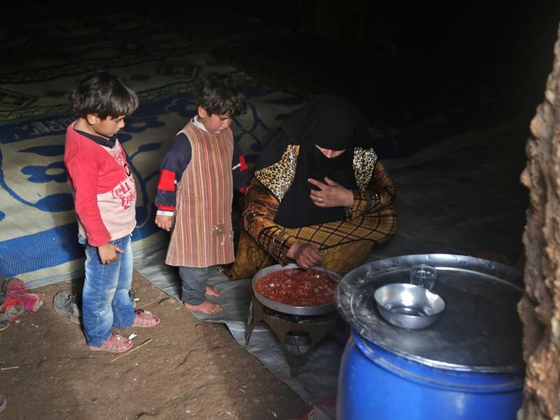 Children stand by a woman preparing food inside an underground shelter where several families of internally displaced Syrians from Aleppo and Idlib provinces are taking refuge, in the village of Taltunah about 15 kilometres northwest of Idlib in the northwestern Idlib province, on February 23, 2020. Aref TAMMAWI / AFP