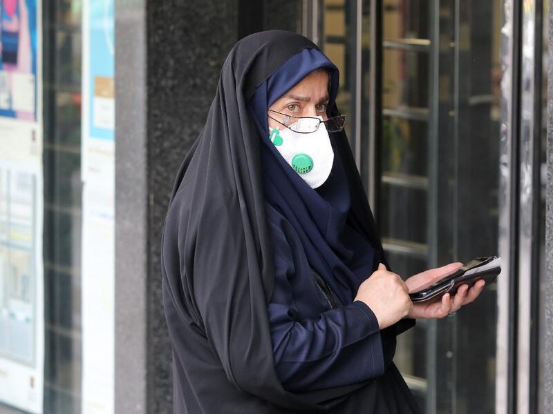 A woman wears a protective mask while using a smartphone as she stands along the side of a street in the Iranian capital Tehran on February 24, 2020. Iran's government vowed on February 24 to be transparent after being accused of covering up the deadliest coronavirus COVID-19 outbreak outside China as it dismissed claims the toll could be as high as 50. The authorities in the Islamic republic have come under mounting public pressure since it took days for them to admit to "accidentally" shooting down a Ukra