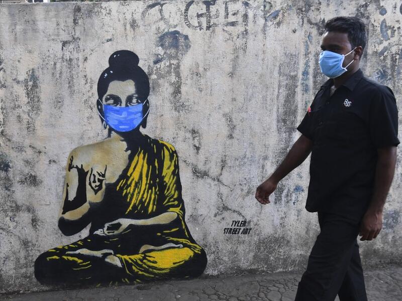 A resident wearing a facemask amid concerns over the spread of the COVID-19 novel coronavirus walks past a graffiti of Buddha wearing facemask, in Mumbai on March 16, 2020. INDRANIL MUKHERJEE / AFP