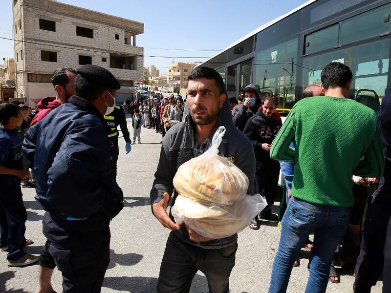People queue to buy subsidised bread from a municipal bus in the Marka suburb in the east of Jordan's capital Amman on March 24, 2020, as the kingdom announced it would deliver bread and water supplies after the government decided to indefinitely extend a curfew amidst efforts to contain COVID-19 coronavirus disease. Jordan imposed a curfew after citizens failed to heed instructions not to leave home except for emergencies, and it has deployed the army to enforce the measure. A fleet of 190 buses chartered 