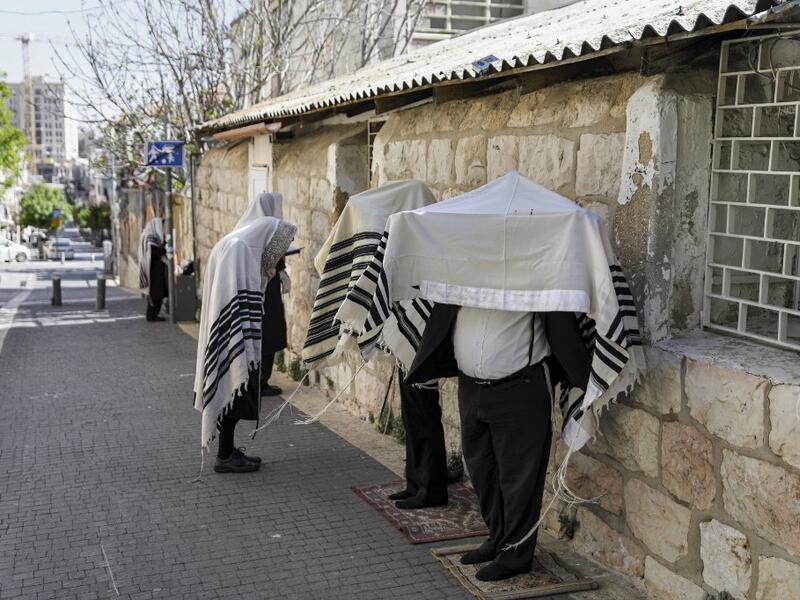 Ultra-Orthodox Jews, wearing the traditional Tallit Jewish prayer shawls, pray along a street outside their closed synagogue in Jerusalem on March 29, 2020, while keeping a distance of two metres from one another following instructions to stop the spread of the COVID-19 coronavirus pandemic. MENAHEM KAHANA / AFP