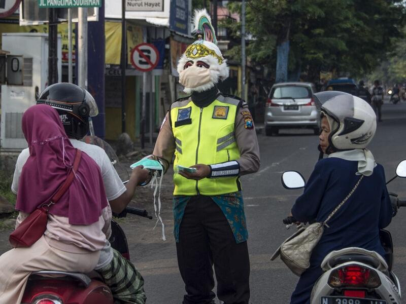 A police officer wearing a Indonesian a superhero costume on the street gives face masks to motorists in Pasuruan, East Java on April 9, 2020, amid concert to the COVID-19 coronavirus. JUNI KRISWANTO / AFP