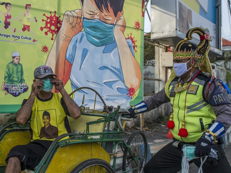 An Indonesian police officer wearing an Indonesian superhero costume on the street gives a face mask to a man in Pasuruan, East Java on April 9, 2020, amid concert to the COVID-19 coronavirus. JUNI KRISWANTO / AFP