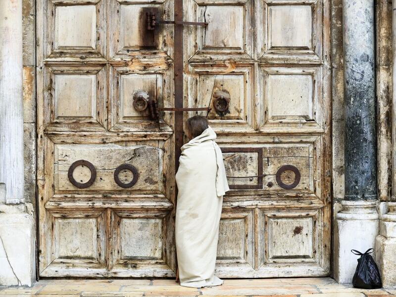 A Christian pilgrim dressed as Jesus Christ stands in front of the closed door of the Holy Sepulchre Church in Jerusalem's Old City on April 10, 2020, marking Good Friday, amid the COVID-19 pandemic crisis. All cultural sites in the Holy Land are shuttered, regardless of their religious affiliation, as authorities seek to forestall the spread of the deadly respiratory disease, which will prevent Christians from congregating for the Easter service, this coming Sunday for Catholic worshippers, then a week lat