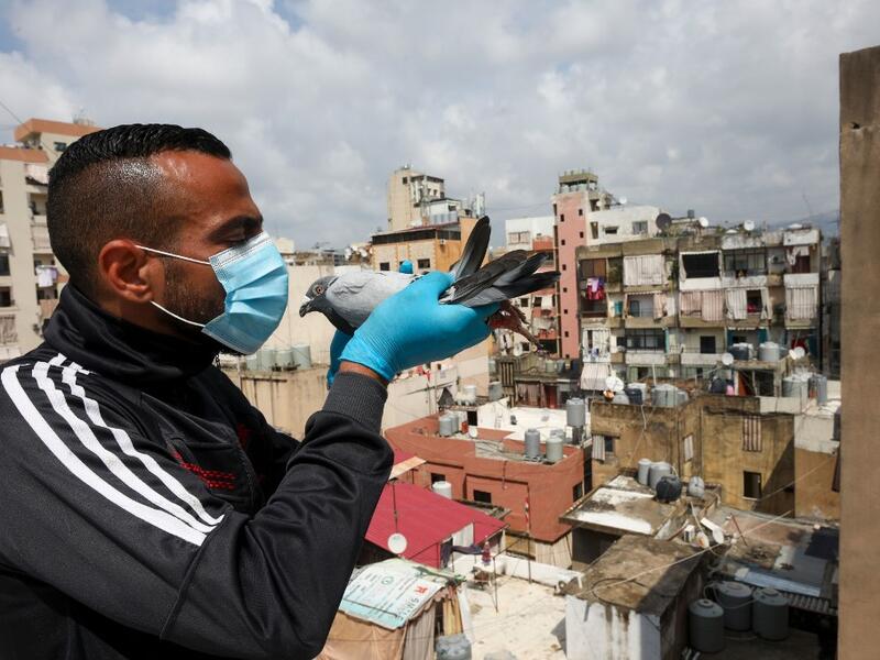 A pigeon owner, wearing personal protective equipment, poses with a pigeon on the rooftop of his building in the southern suburb of Beirut on April 11, 2020. ANWAR AMRO / AFP