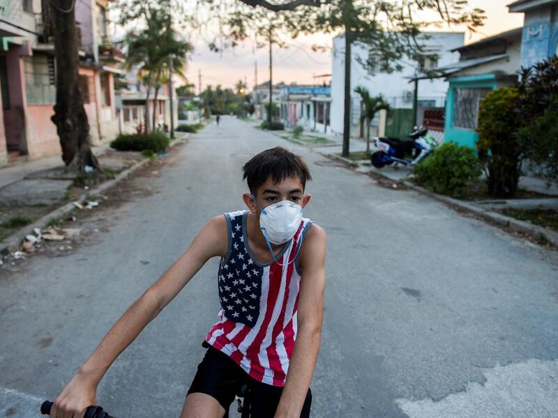 A youngster wearing a shirt with the US flag and a face mask, rides a bicycle in Havana, on April 13, 2020. While Cuba tries to stop the spread of the coronavirus on the island, with 726 cases, voices can be heard to demand the lifting of the US embargo to facilitate the arrival of medical products. YAMIL LAGE / AFP
