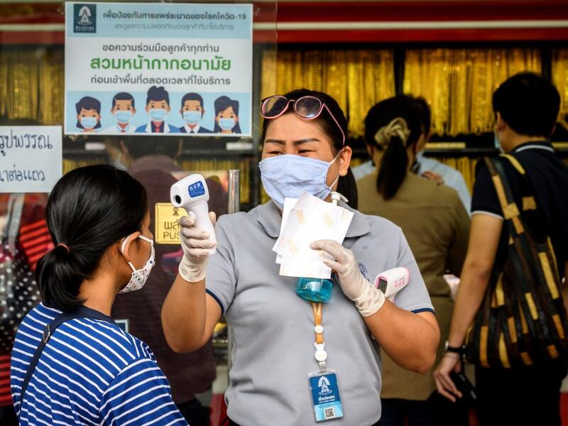 An employee wearing a face mask amid fears of the spread of COVID-19 coronavirus checks the temperature of a customer outside a gold shop in Bangkok's Chinatown on April 15, 2020. Hundreds of Bangkok residents rushed to goldsmith shops in order to sell their jewelries as gold prices reached its highest levels since 2012. Mladen ANTONOV / AFP