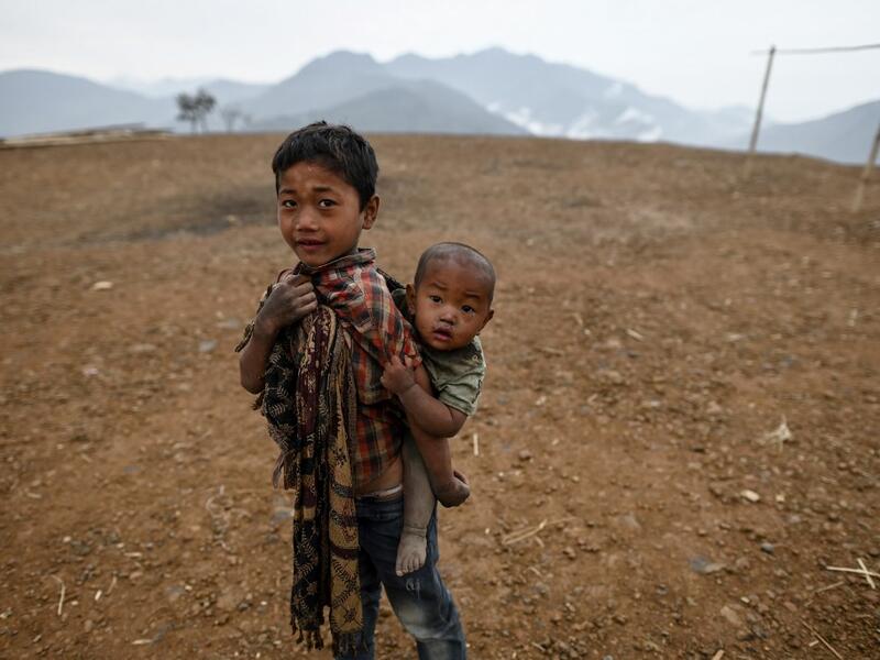 This photo taken on February 9, 2020 shows a boy carrying his brother in front of their house in Karmawlawyi village in Myanmar's Sagaing region, near the border with India. The king of the Konyak tribe sleeps in Myanmar, but eats in India -- his house, village and people divided by a mountain border which serves as a vulnerable lifeline now severed by a coronavirus lockdown.  Ye Aung THU / AFP