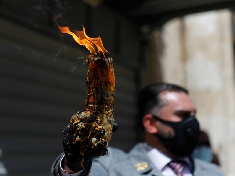 A man wearing a protective mask holds up candles lit from the Holy Fire in the church of the Holy Sepulchre, as very few Orthodox Christians gather in Jerusalem's Old City to celebrate Easter due to the lockdown imposed by authorities in a bid to limit the spread of the novel coronavirus, on April 18, 2020. Ahmad GHARABLI / AFP