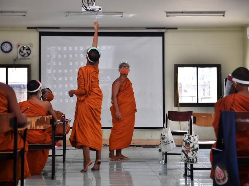 A novice monk wearing a face shield as a preventive measure against the spread of the COVID-19 coronavirus turns off a projector during religious studies at Wat Molilokkayaram Buddhist temple in Bangkok on April 20, 2020. Lillian SUWANRUMPHA / AFP