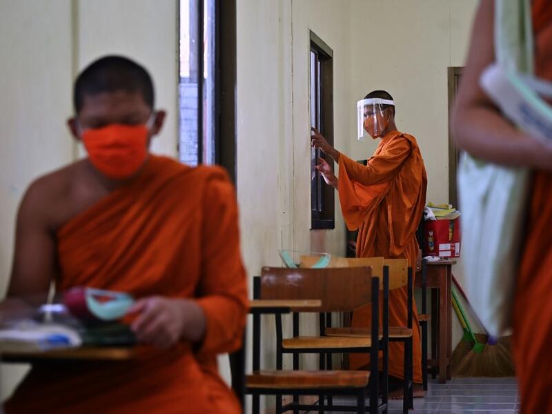 A novice monk wearing a face shield as a preventive measure against the spread of the COVID-19 coronavirus closes the window of a classroom before religious studies at Wat Molilokkayaram Buddhist temple in Bangkok on April 20, 2020. Lillian SUWANRUMPHA / AFP