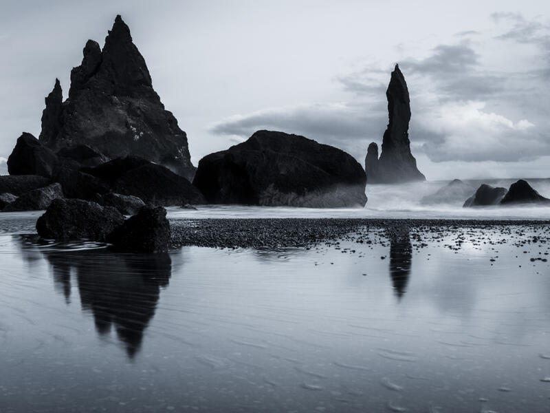Rock formations on a black sand beach in Iceland with reflection in the Sea and a dark sky in misty moody weather with dark colors and a rough sea (Shutterstock)