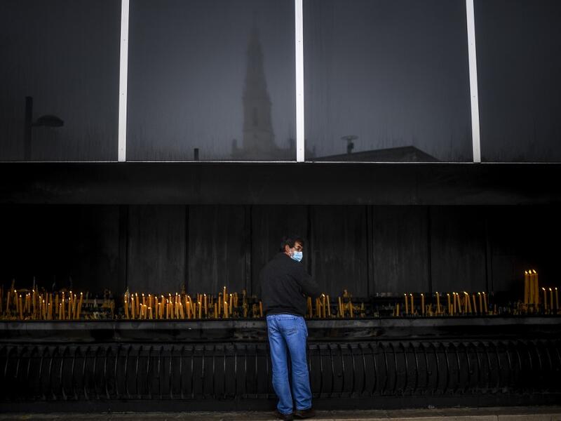 A man wearing a face mask lights a candle during the 103rd anniversary of the apparitions of Our Lady of Fatima at the Fatima shrine in central Portugal on May 13, 2020. Without the crowd of pilgrims it welcomes every year, the shrine of Fatima celebrated the anniversary during a religious ceremony reduced to the bare minimum. PATRICIA DE MELO MOREIRA / AFP