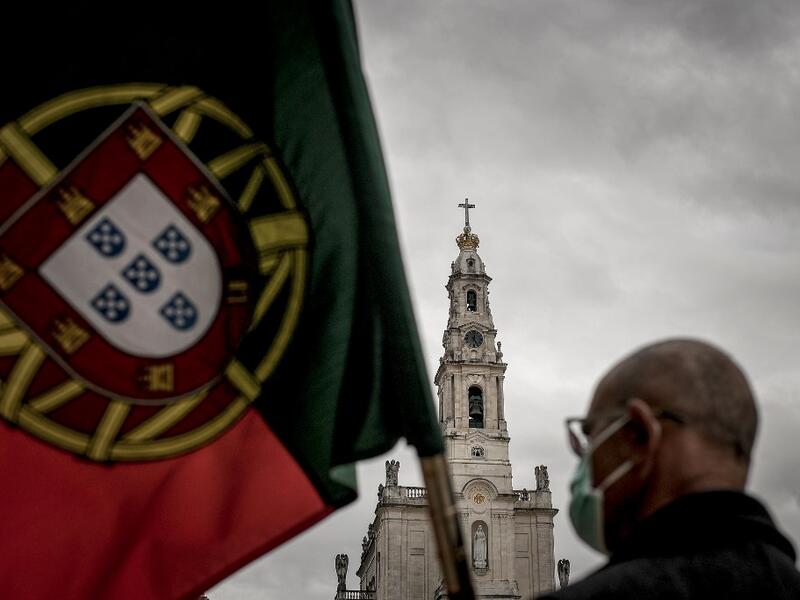 A man holds a Portuguese flag during the 103rd anniversary of the apparitions of Our Lady of Fatima at the Fatima shrine in central Portugal on May 13, 2020. Without the crowd of pilgrims it welcomes every year, the shrine of Fatima celebrated the anniversary during a religious ceremony reduced to the bare minimum. PATRICIA DE MELO MOREIRA / AFP