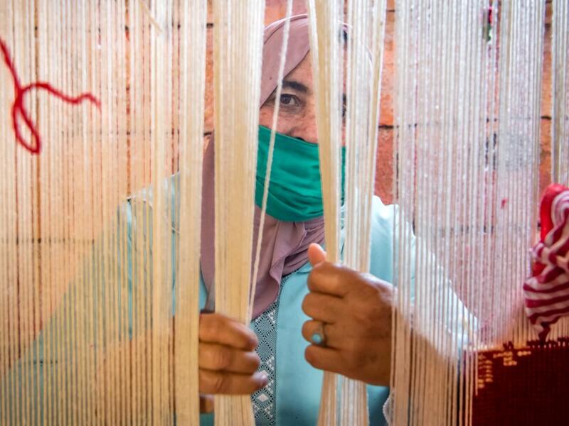 A Moroccan rug weaver peeks from behind carpet thread at a workshop in the city of Sale, north of the capital Rabat, on June 3, 2020, during the novel coronavirus pandemic. Artisans in Morocco have been starved of income for almost three months because of the COVID-19 pandemic. The crafts industry represents some seven percent of GDP, with an export turnover last year of nearly 1 billion dirhams ($100 million). FADEL SENNA / AFP