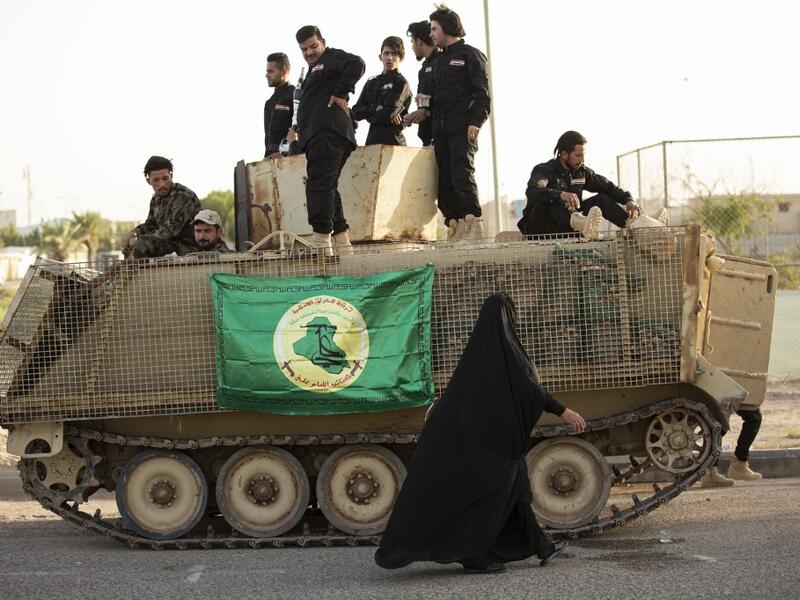 A woman walks past members of the Hashed al-Shaabi (Popular Mobilisation) paramilitary force taking part in a military parade in the southern Iraqi city of Basra on June 14, 2020, marking the sixth anniversary of its founding after Iraq's top Shiite cleric Grand Ayatollah Ali Sistani called to defend the country from the Islamic State group (IS). Hussein FALEH / AFP